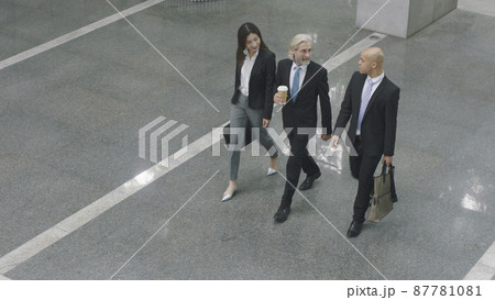 high angle view of three corporate executives talking while walking across lobby of modern office building 87781081
