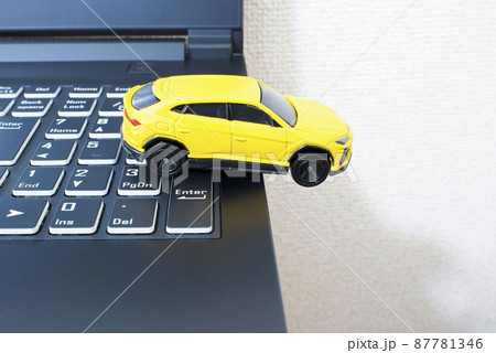 黒いパソコンのキーボードの上で単独事故を起こして脱輪している黄色いミニカー 87781346