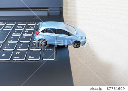 黒いパソコンのキーボードの上で単独事故を起こして脱輪している水色のコンパクトカー 87781609