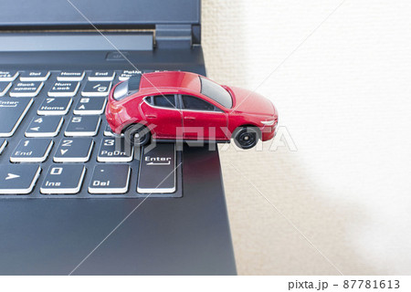 黒いパソコンのキーボードの上で単独事故を起こして脱輪している赤いミニカー 87781613