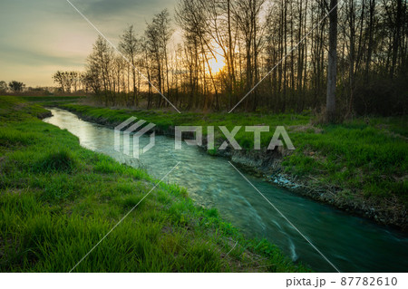 A small river and sunset behind the trees A small river and sunset behind the trees 87782610