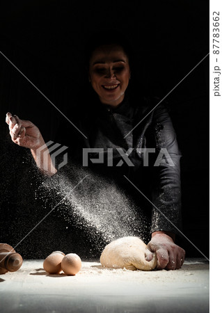 women kneads dough and scatters flour on a black background. 87783662