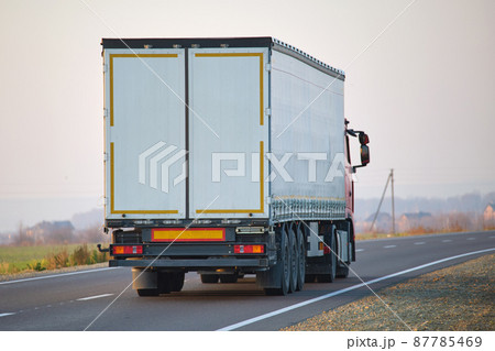 Semi-truck with cargo trailer driving on highway hauling goods in evening. Delivery transportation and logistics concept Semi-truck with cargo trailer driving on highway hauling goods in evening. Delivery transportation and logistics concept 87785469