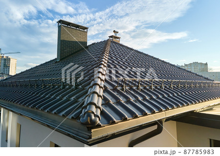 Closeup snow guard for safety in winter on house roof top covered with ceramic shingles. Tiled covering of building 87785983