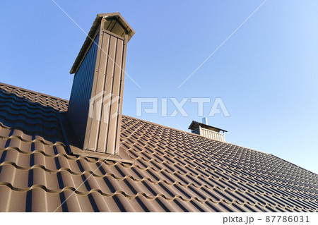 Chimney on house roof top covered with metallic shingles under construction. Tiled covering of building. Real estate development Chimney on house roof top covered with metallic shingles under construction. Tiled covering of building. Real estate development 87786031