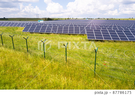 Aerial view of solar power plant on green field with protective wire fence around it. Electric panels for producing clean ecologic energy. Aerial view of solar power plant on green field with protective wire fence around it. Electric panels for producing clean ecologic energy. 87786175