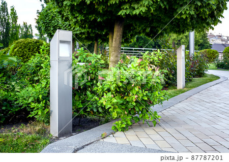 modern iron lantern of ground garden led lighting with bushes in city street with trees near flower bed landscape near brick stone tile pedestrian walkway with granite curb, nobody. 87787201