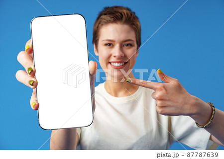 Portrait of a young woman showing blank screen mobile phone while standing over blue background 87787639