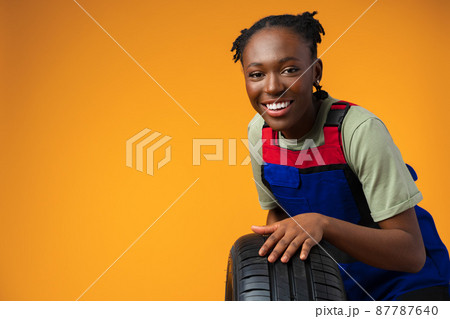 Portrait of smiling black female mechanic posing with new car tyres in studio 87787640