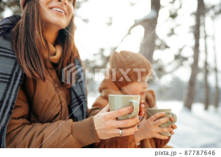 Young woman with a son in winter forest on a picnic drink hot tea 87787646