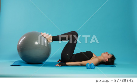 Fit adult using fitness toning ball to train legs muscles in front of camera 87789345
