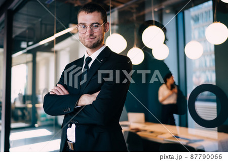 Positive businessman standing with arms folded in business center Positive businessman standing with arms folded in business center 87790066