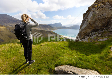 Woman hiking in high mountains and looking at Haukland Beach at Vestvagoy Island at Lofoten, Norway 87790318