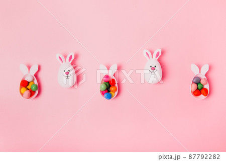 Top view festive Easter pink background with funny bunny eggs container filled with candy chocolate eggs. Bunny rabbit symbol. Easter egg hunt. Creative Easter. Flat lay. Copy space 87792282