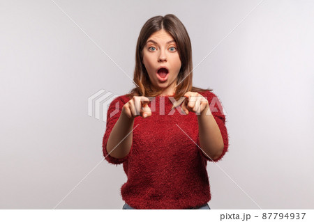 Wow, hey you. Portrait of amazed shocked brunette woman in shaggy sweater pointing finger to camera, looking with surprise, noticing and making choice. indoor studio shot isolated on gray background 87794937