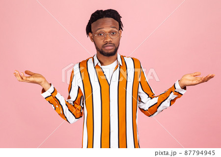 I don't know. Puzzled confused bearded afro-american man with dreadlocks in eyeglasses and striped shirt shrugging shoulders, uncertain, has no answer. Indoor studio shot isolated on pink background. I don't know. Puzzled confused bearded afro-american man with dreadlocks in eyeglasses and striped shirt shrugging shoulders, uncertain, has no answer. Indoor studio shot isolated on pink background. 87794945