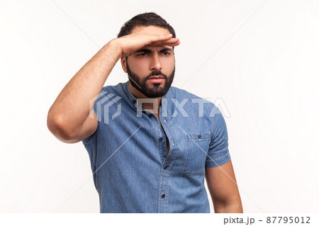 Thoughtful bearded man looking far away at distance with hand over head, attentively searching for bright future. Indoor studio shot isolated on white background 87795012