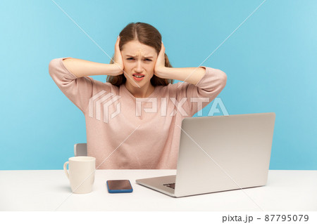 Don't want to listen anymore. Irritated woman employee sitting at workplace with laptop, covering ears and frowning displeased, annoyed by noisy sound. indoor studio shot isolated on blue background 87795079