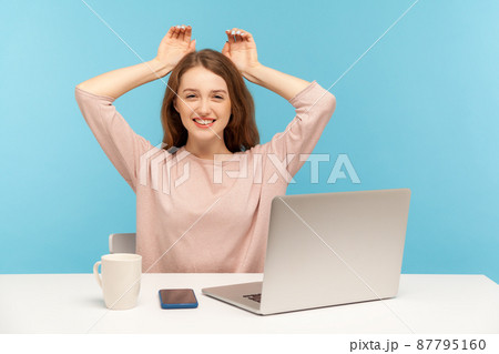 Charming young woman employee smiling and showing bunny ears on head, resting, having fun at workplace in home office, feeling carefree and happy. indoor studio shot isolated on blue background 87795160