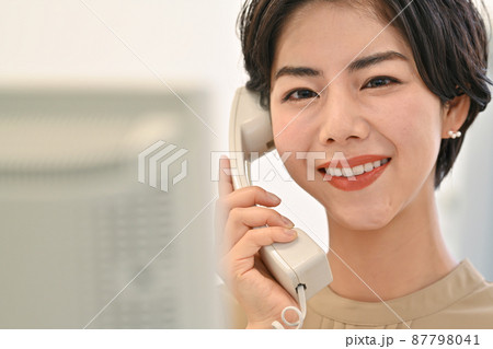 オフィスでディスクのパソコンの前で電話をする女性 87798041