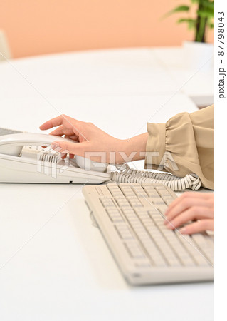 キーボードを打ちながら受話器に手を伸ばす女性の手元 キーボードを打ちながら受話器に手を伸ばす女性の手元 87798043