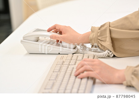 キーボードを打ちながら受話器に手を伸ばす女性の手元 87798045