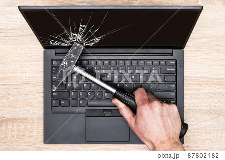 Hand breaking laptop screen with a hammer 87802482