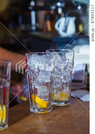 cubes of ice in glass with slice of lemon on bar. cocktail cubes of ice in glass with slice of lemon on bar. cocktail 87803217
