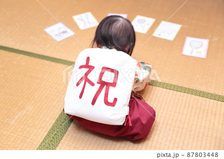 1歳の誕生日に袴を着て一升餅を背負って選び取りをする子供 87803448