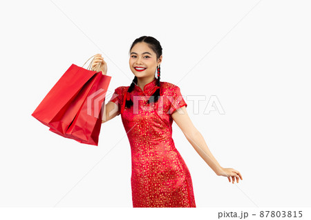 Chinese new year in shopping concept, Asian girl in red cheongsam costume smiling and holding shopping bags isolated on white background. 87803815
