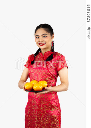 Asian girl in red traditional oriental dress holding plate of oranges isolated on white background. Chinese new year concept style.. 87803816