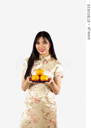 Chinese new year concept style. Asian woman in gold traditional oriental dress holding a plate of oranges on white background.. 87803818
