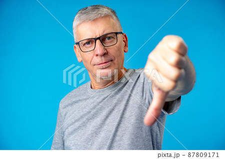 Portrait of mature man showing thumbs down sign gesture, standing on blue backgorund Portrait of mature man showing thumbs down sign gesture, standing on blue backgorund 87809171