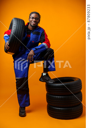 African american car service worker with car tyre against yellow background 87809233