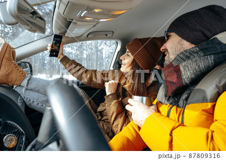 Family couple sitting in car in winter clothes iin snow forest 87809316