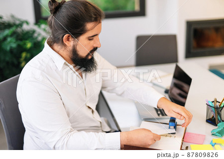 Young entrepreneur stapling papers while working at home. Young entrepreneur stapling papers while working at home. 87809826