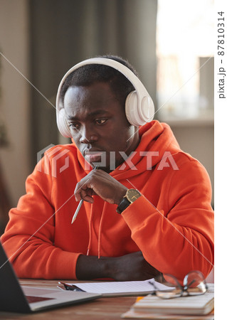 Vertical portrait shot of concentrated university student wearing headphones sitting at desk watching online lesson on laptop 87810314