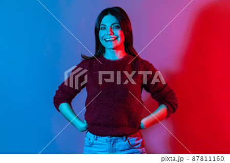Neon light portrait of happy lovely beautiful brunette woman in pullover standing confident and looking at camera with toothy smile, enjoying life, positive outlook. indoor studio shot isolated 87811160