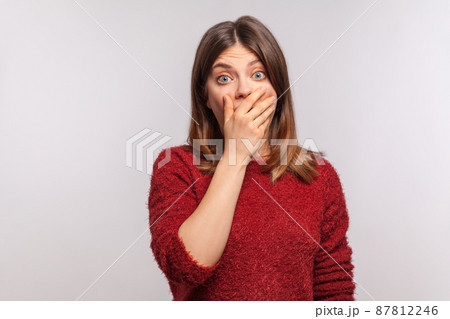I won't say anything to anyone. Portrait of scared brunette girl in shaggy sweater put mouth on hand and looking with fear in her eyes, keeping terrible secret. studio shot isolated on gray background 87812246