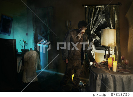 Eerie zombie man standing near dining table Eerie zombie man standing near dining table 87813739