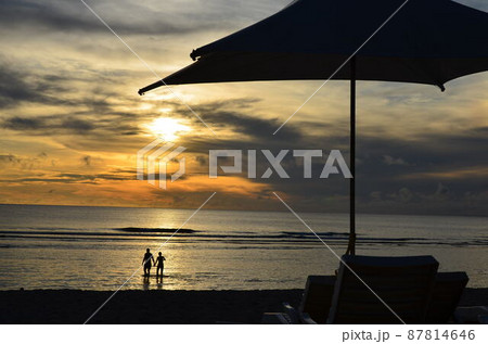 浜辺からみた夕日とカップルとビーチパラソル1 87814646