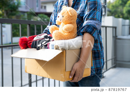 Holding clothing donation box with used clothes and doll at home to support help for poor people in the world. 87819767