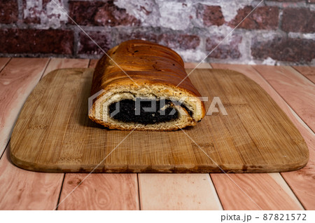Homemade roll with poppy seeds on a wooden board on the table. 87821572