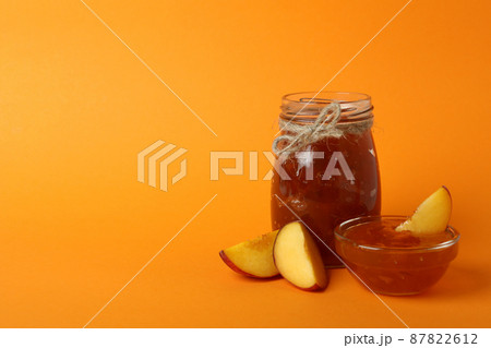 Jar and bowl of peach jam and ingredients on orange background 87822612