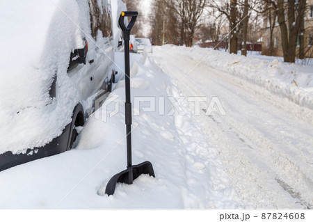 Plastic snow shovel in front of snow-covered minivan at sunny winter morning 87824608