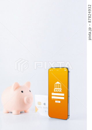 Mobile banking. Smartphone with internet online bank application. Piggy bank with debit card on white background. Save money business concept. 87824932
