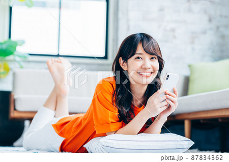 リビングでスマホを持つ若い女性 87834362