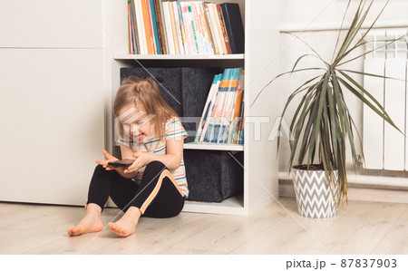 Little girl in the room sits and looks at the phone Little girl in the room sits and looks at the phone 87837903