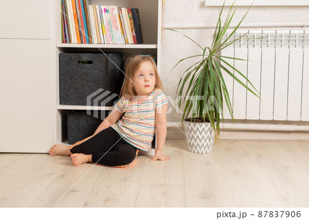 Child sits on the floor in the room near the bookcase Child sits on the floor in the room near the bookcase 87837906