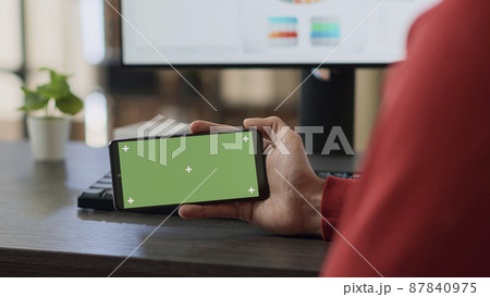Businessman using horizontal green screen on smartphone, looking at isolated mockup copyspace with blank chroma key background. Office employee working with template on mobile phone. Close up. 87840975